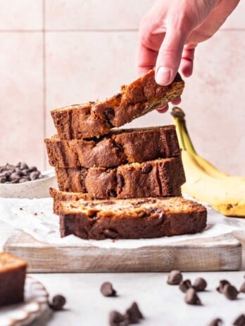 3 slices of banana bread piled on top of each other and a hand taking on slice off the top