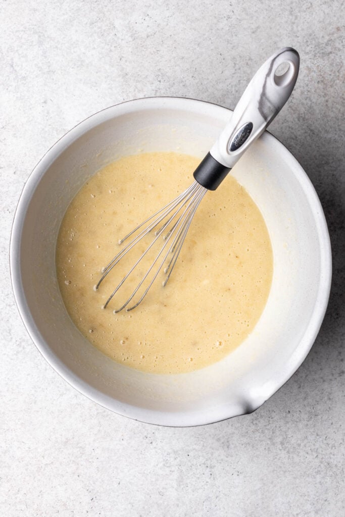 oil, eggs and sugar mixed in a white bowl with a whisk