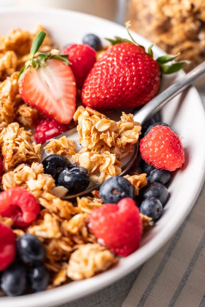 a spoon with granola, milk and berries in a bowl