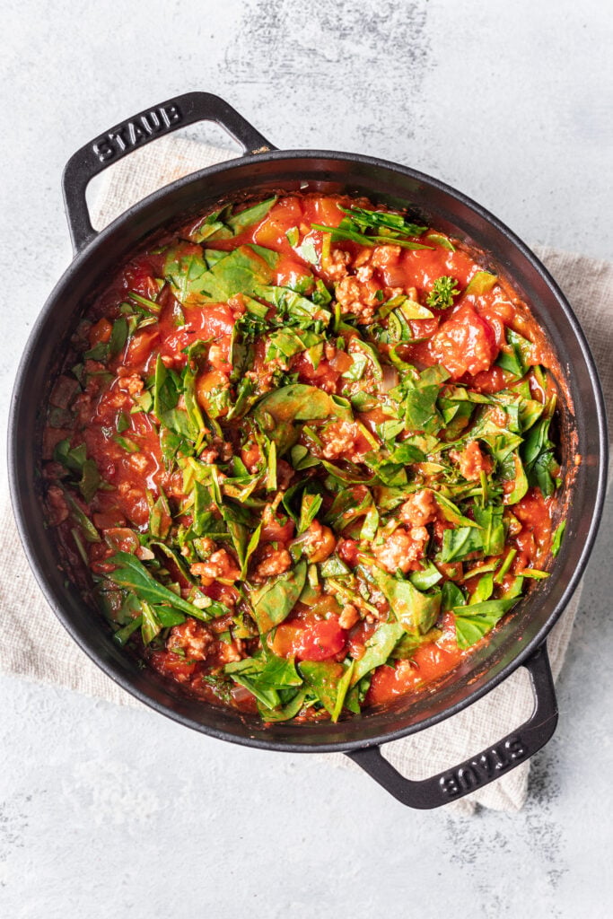 pasta in a skillet with sauce and spinach