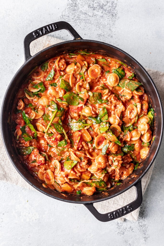 pasta in a skillet with sauce and spinach