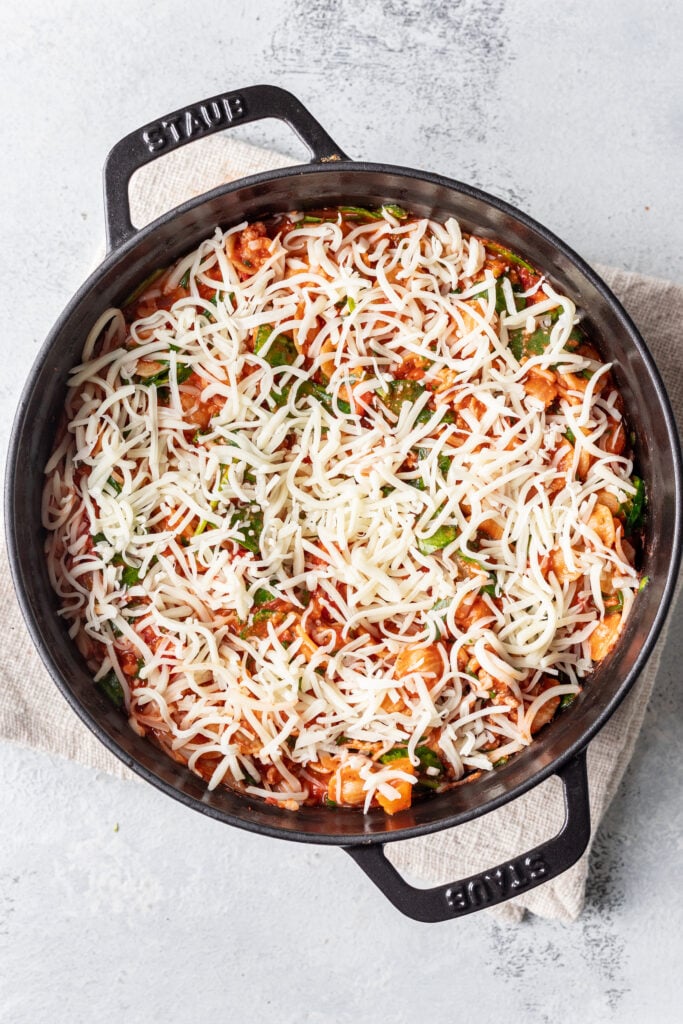 pasta in a skillet with shredded cheese on top