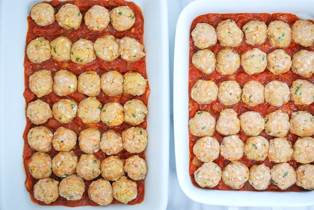 overhead shot of uncooked meatballs in baking dish sitting on top of tomato sauce