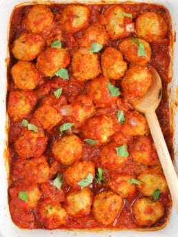 overhead shot of meatballs in a baking dish with a wooden spoon and tomato sauce