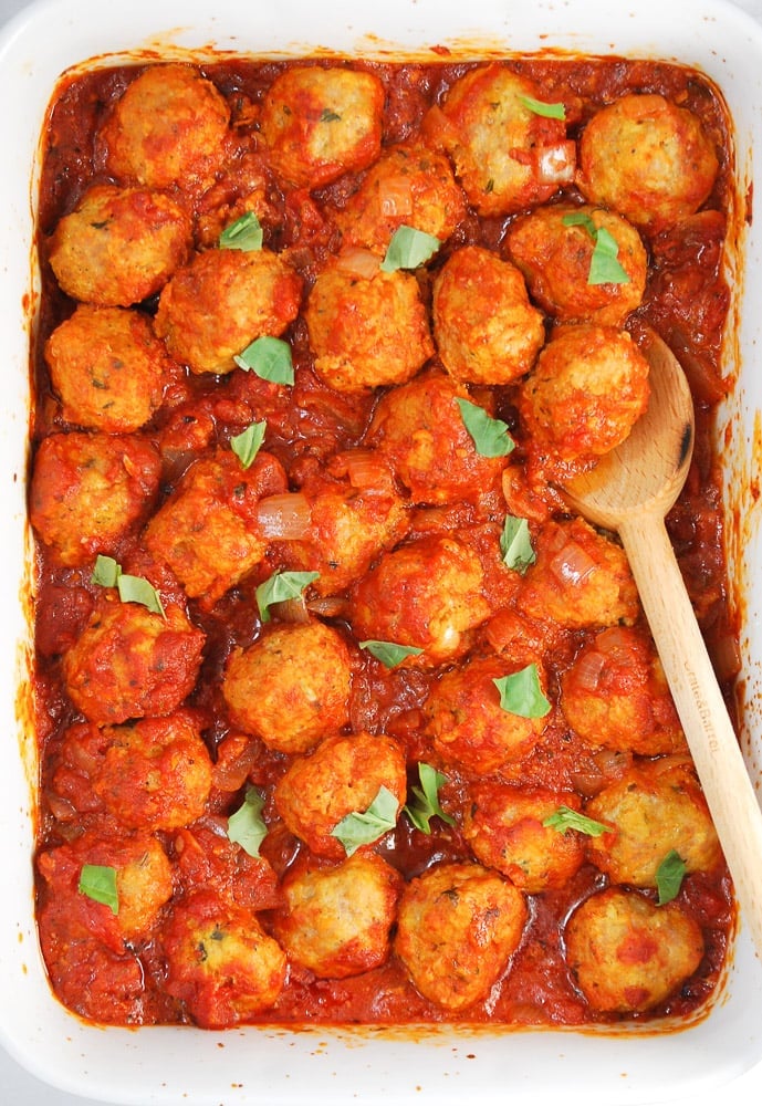 overhead shot of meatballs in a baking dish with a wooden spoon and tomato sauce