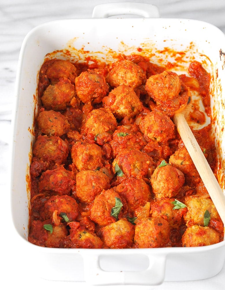meatballs in a baking dish with a wooden spoon and tomato sauce