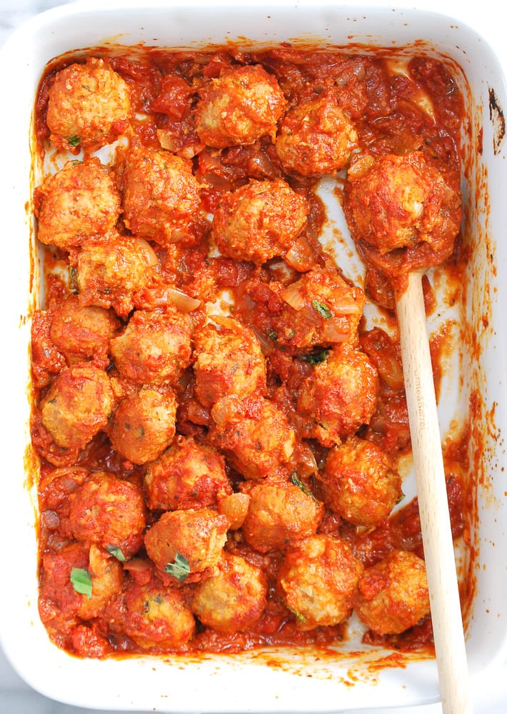 overhead shot of meatballs in a baking dish with a wooden spoon and tomato sauce