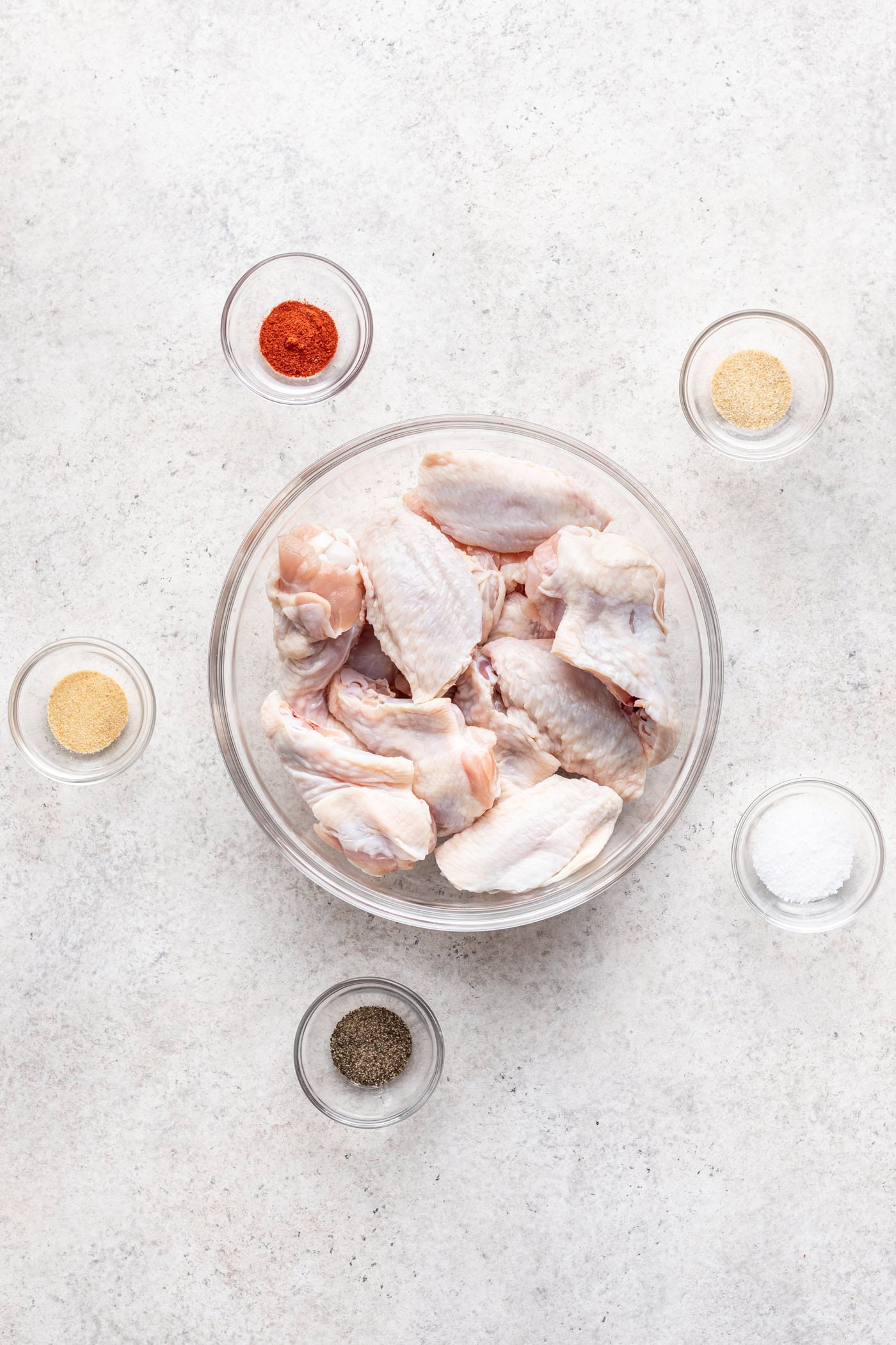 bowls of ingredients including raw chicken wings and small bowls of spices