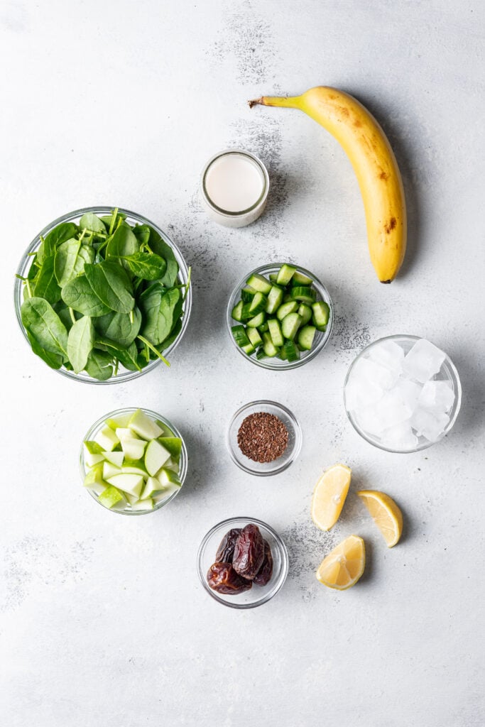 ingredients in bowls like spinach, cucumber, apple, lemon, dates