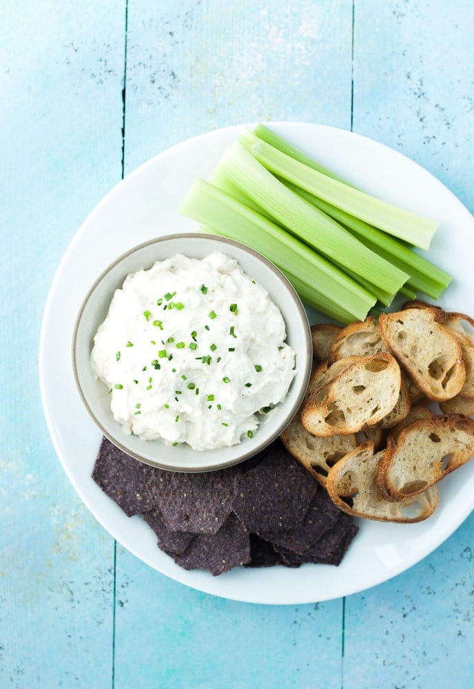 crab dip in a bowl with celery sticks, crostini and blue chips