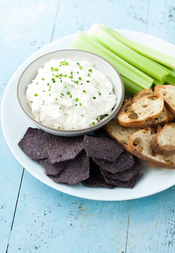crab dip in a bowl with celery sticks, crostini and blue chips