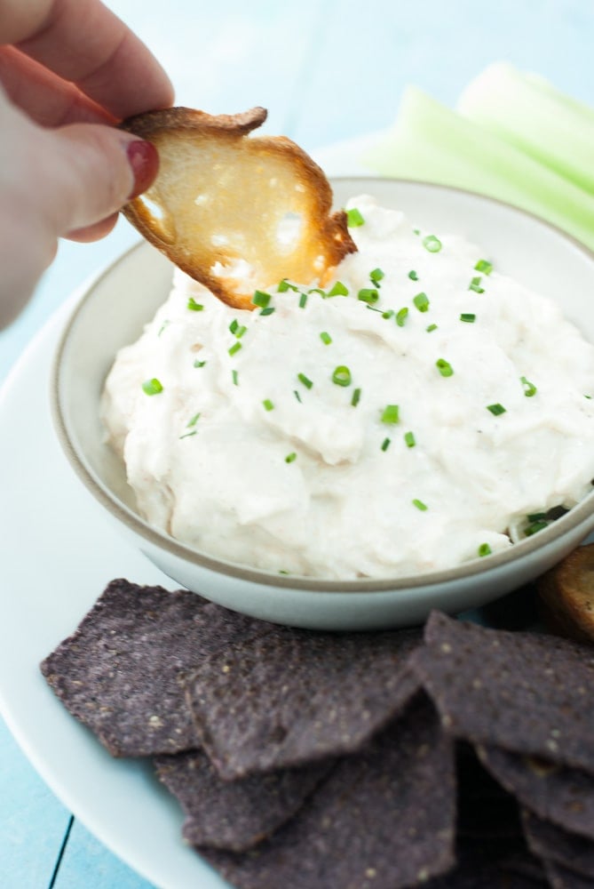 crostini dipping into crab dip with chives on top