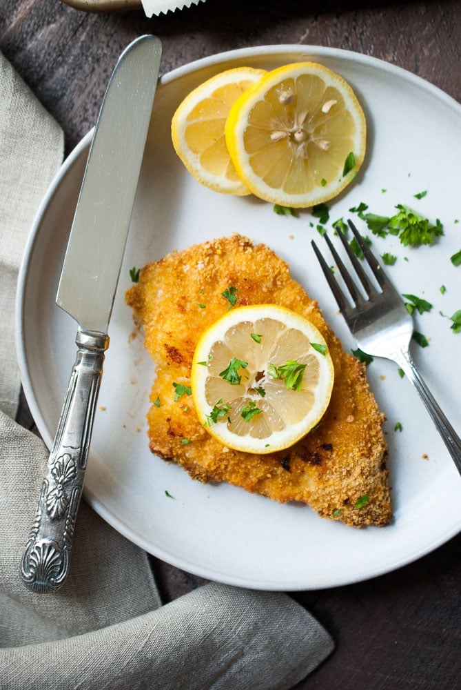 breaded chicken cutlet on a plate with a knife and fork