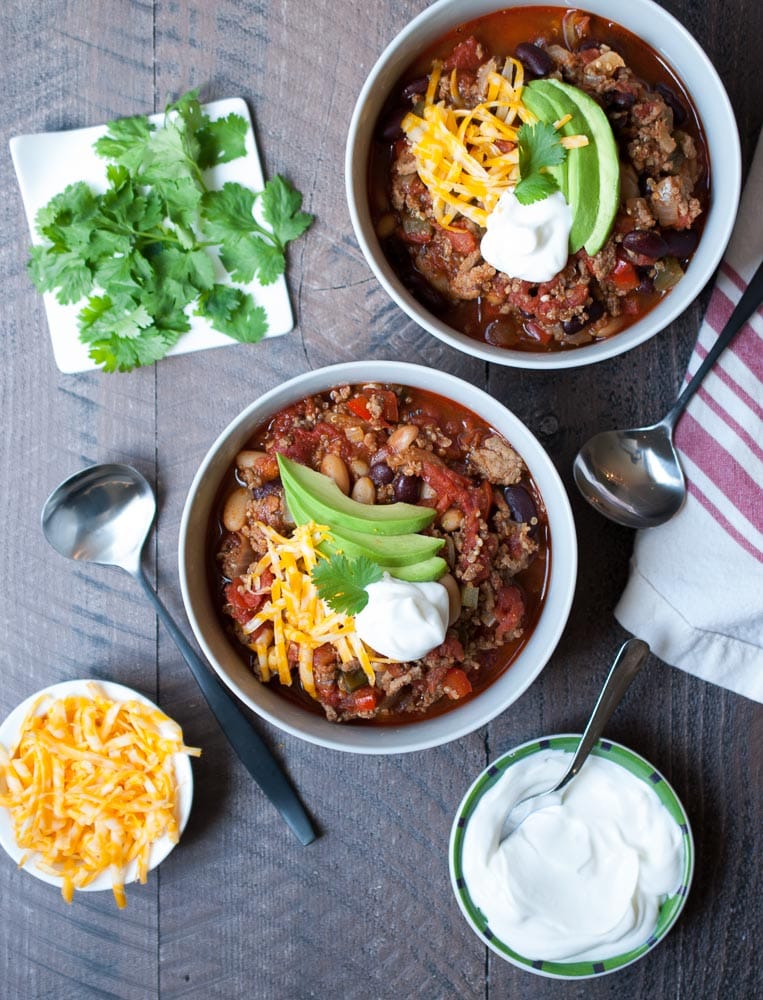 overhead shot of two bowls of chili with a dollop of sour cream, avocado and cheese