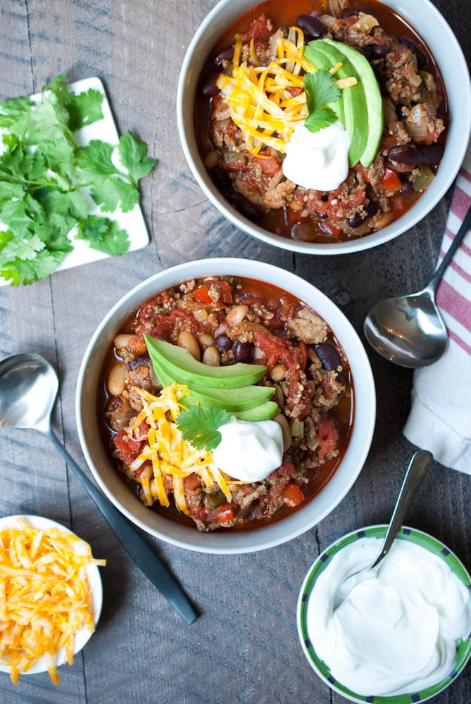 overhead shot of two bowls of chili with a dollop of sour cream, avocado and cheese
