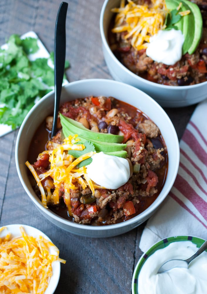overhead shot of a bowl of chili with a dollop of sour cream, avocado and cheese and a spoon in it