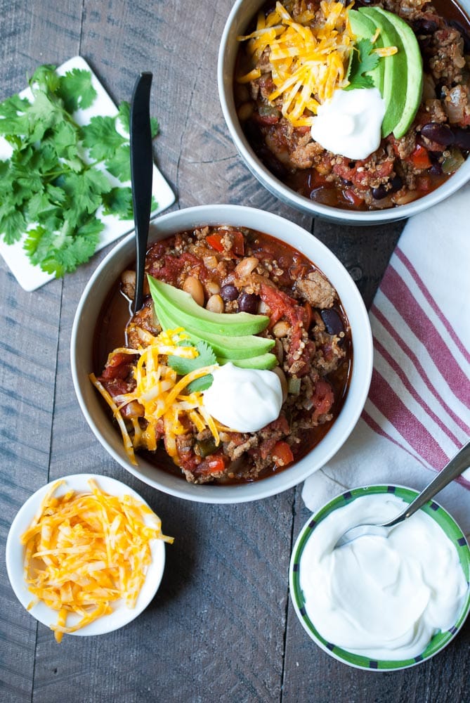 overhead shot of two bowls of chili with a dollop of sour cream, avocado and cheese