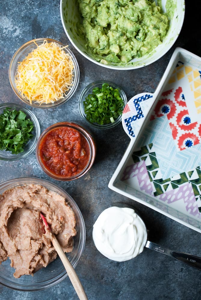 ingredients in a bowl such as guacamole, cheese, salsa, cilantro and scallions