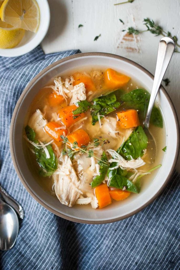 Chicken soup in a bowl with a spoon with a side of sliced lemons