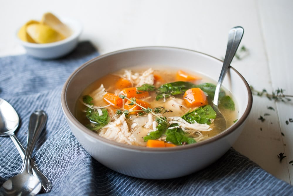 Chicken soup in a bowl with a spoon with a side of sliced lemons