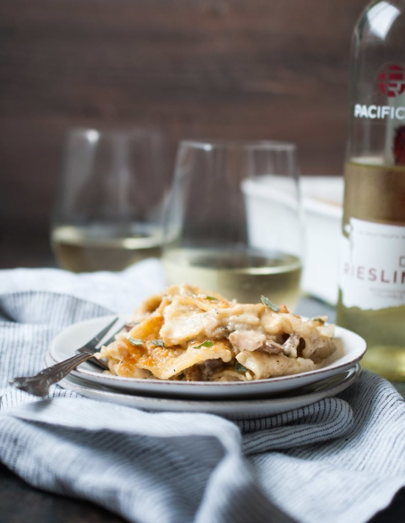 Mushroom Sage Lasagna on a plate with a fork and a glass of wine in the background