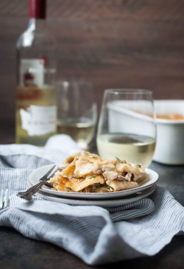 Mushroom Sage Lasagna on a plate with a fork and a glass of wine in the background