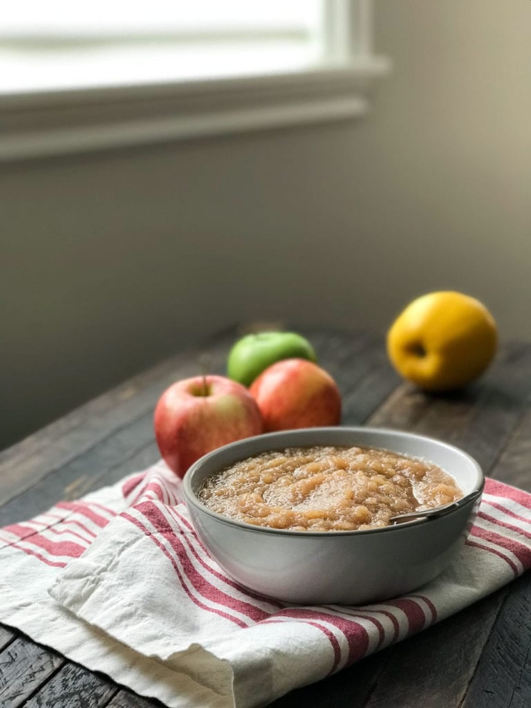 bowl of applesauce with spoon resting in it, on red and white napkin and apple scattered around