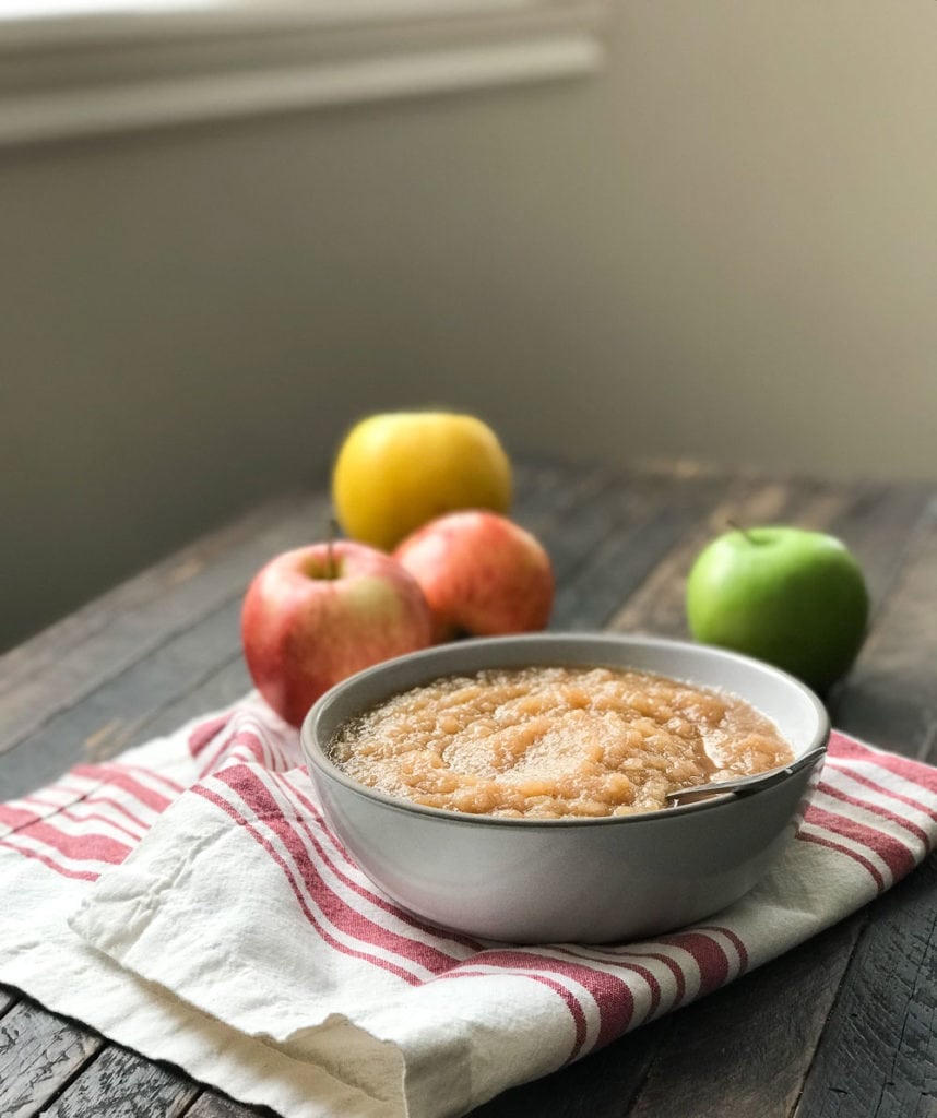 bowl of applesauce with spoon resting in it, on red and white napkin and apple scattered around