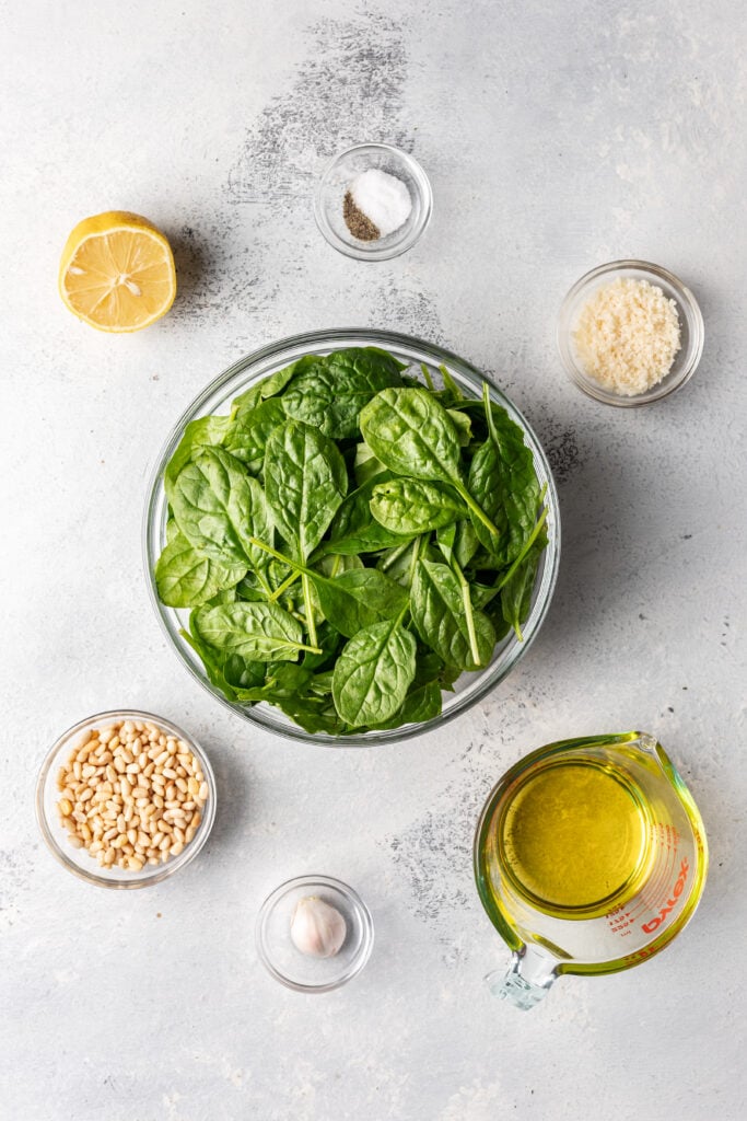 bowls of ingredients on a board like spinach, oil, pine nuts, parmesan cheese and lemon