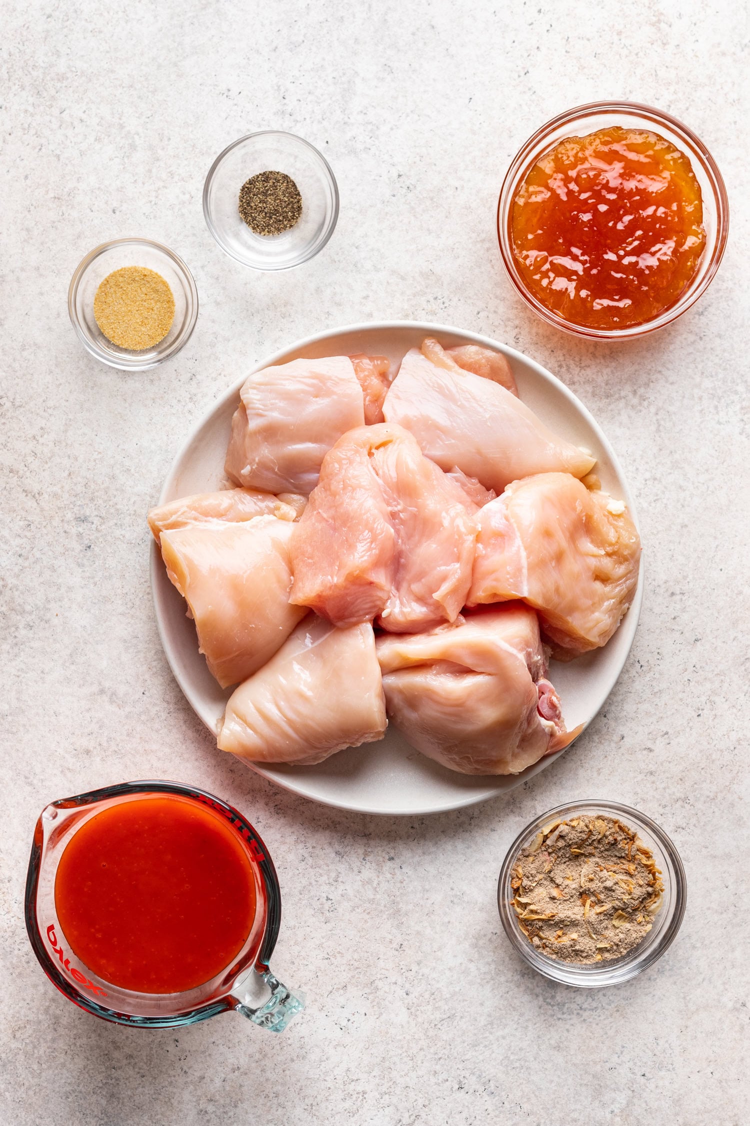 raw chicken on a plate with bowls of ingredients around