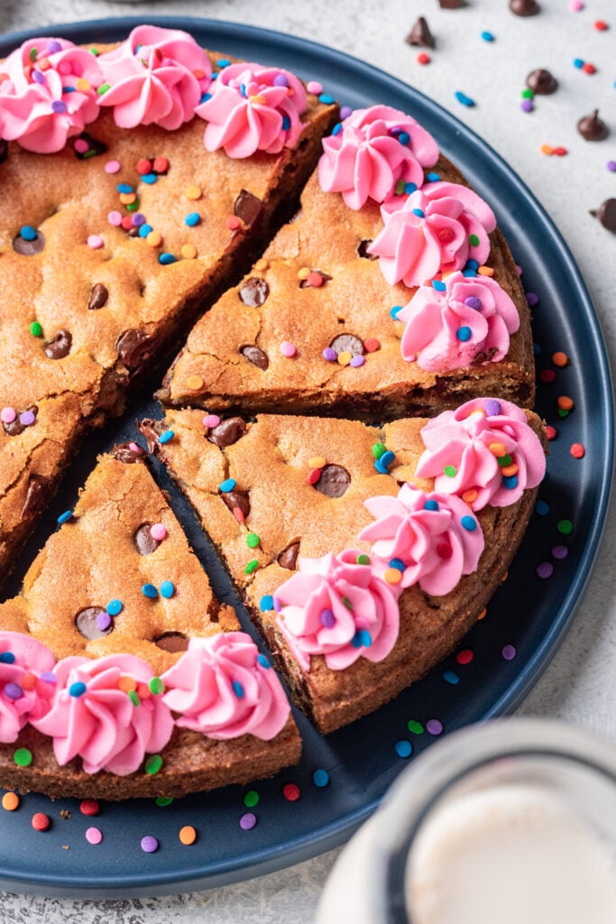 cookie cake with pink piped frosting and sprinkles cut into slices