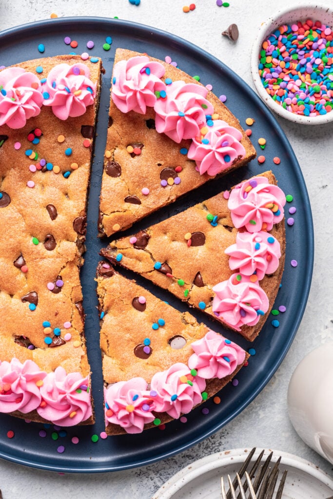 cookie cake with pink piped frosting and sprinkles cut into slices