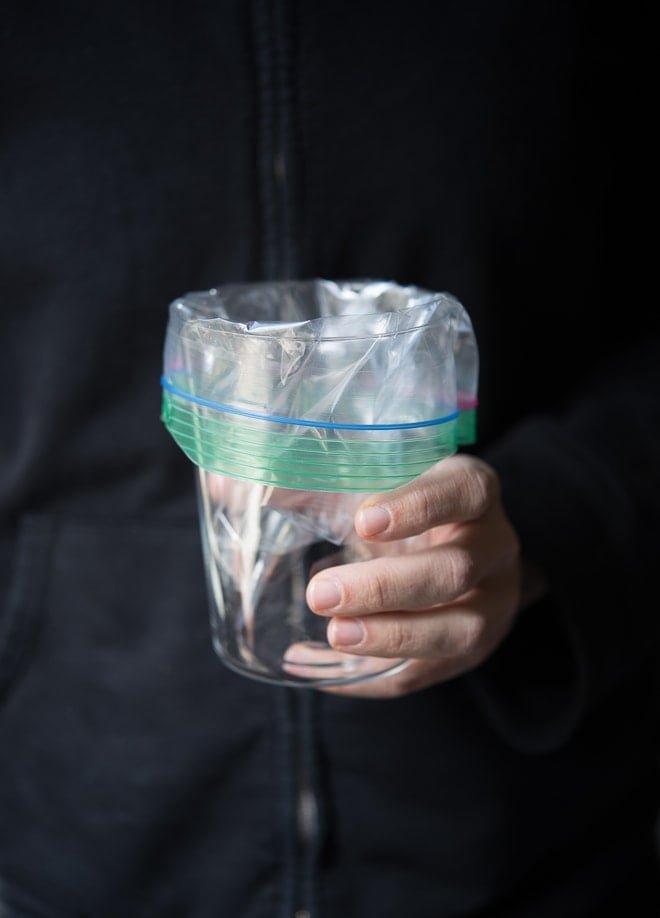 Hand holding a glass with a plastic bag inserted and folded over the edges