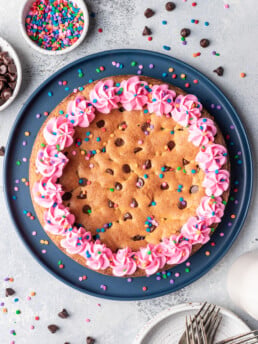cookie cake with pink piped frosting and sprinkles on a blue plate