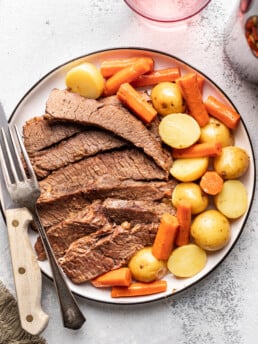 sliced brisket with carrots and potatoes and a serving fork on a platter