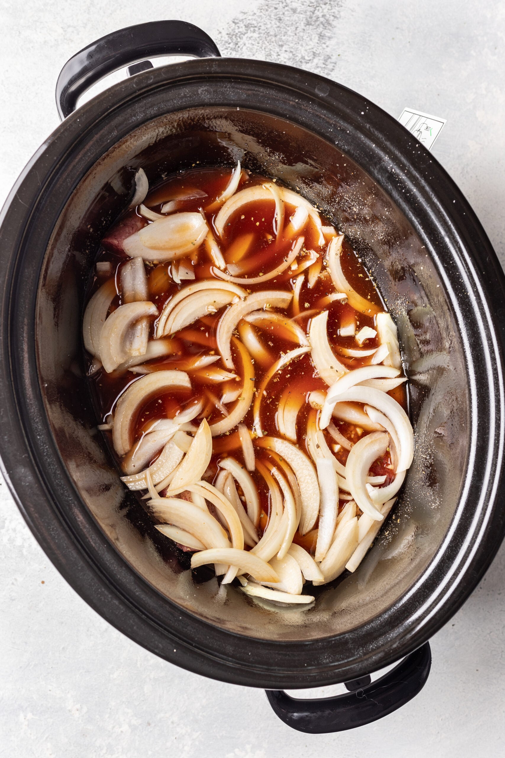 slow cooker with a brisket covered in sliced onions and broth