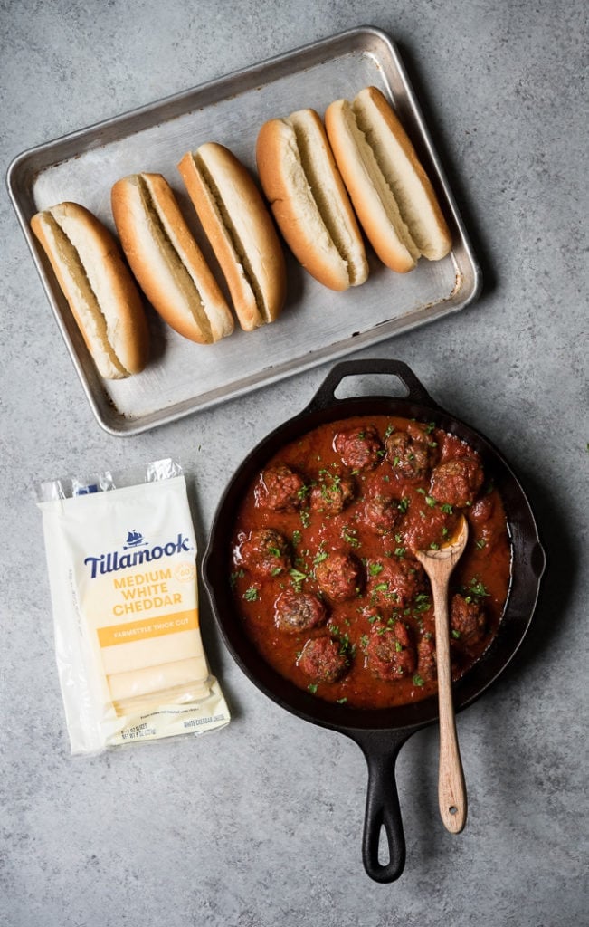 cooked meatballs in a cast iron skillet with sauce and some buns and a package of cheese on the side