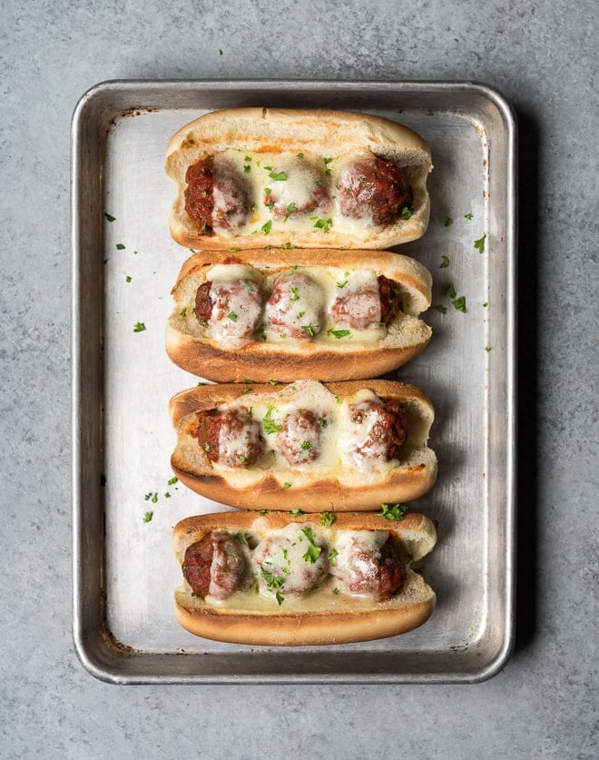 overhead shot of 4 meatball subs with melted cheese on a sheet pan