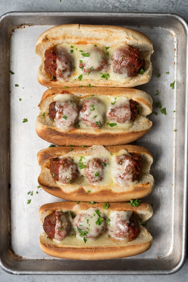 overhead shot of 4 meatball subs with melted cheese on a sheet pan