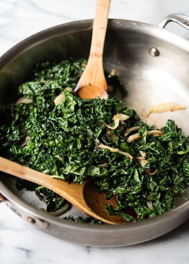 sauteed kale and fennel in a pan with wooden spoons