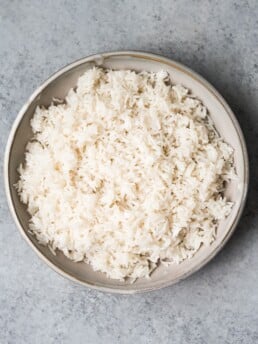 overhead shot of cooked coconut rice in a bowl on a grey background