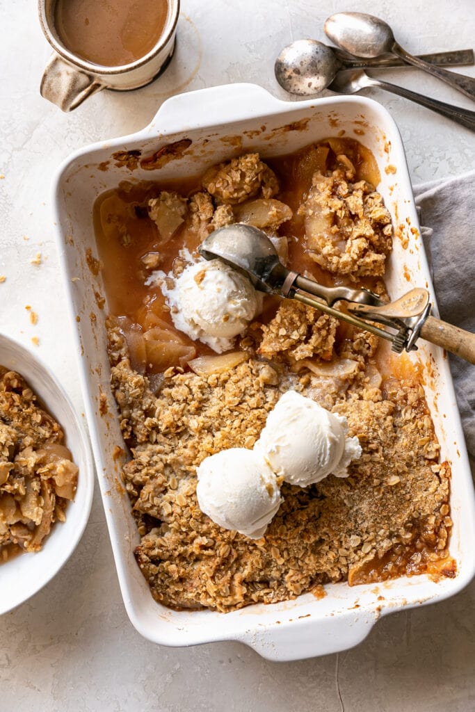 overhead apple crisp in rectangular pan with three scoops of vanilla ice cream and coffee