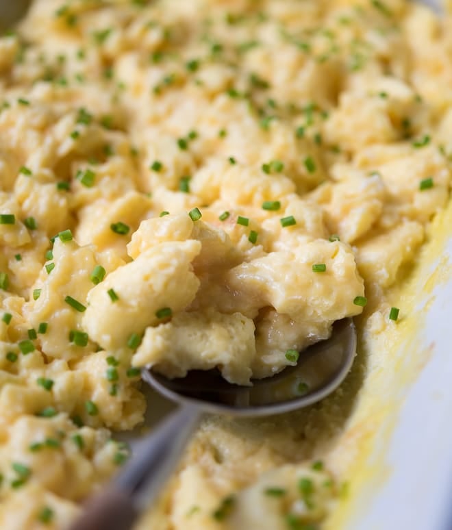 Scrambled Eggs sprinkled with chives being scooped with a spoon