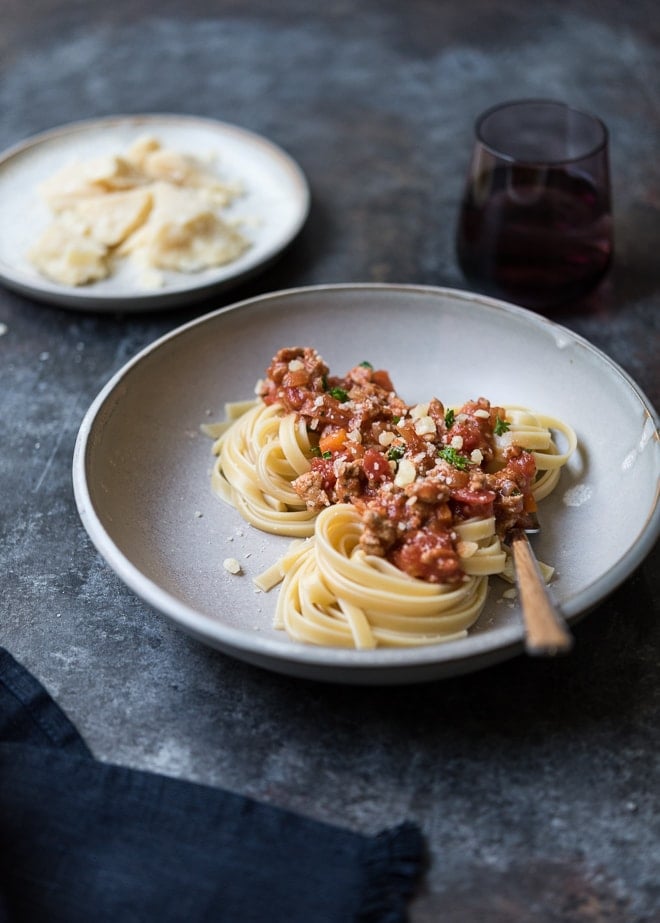 turkey bolognese served over fettucine on a plate with a fork and a wine glass