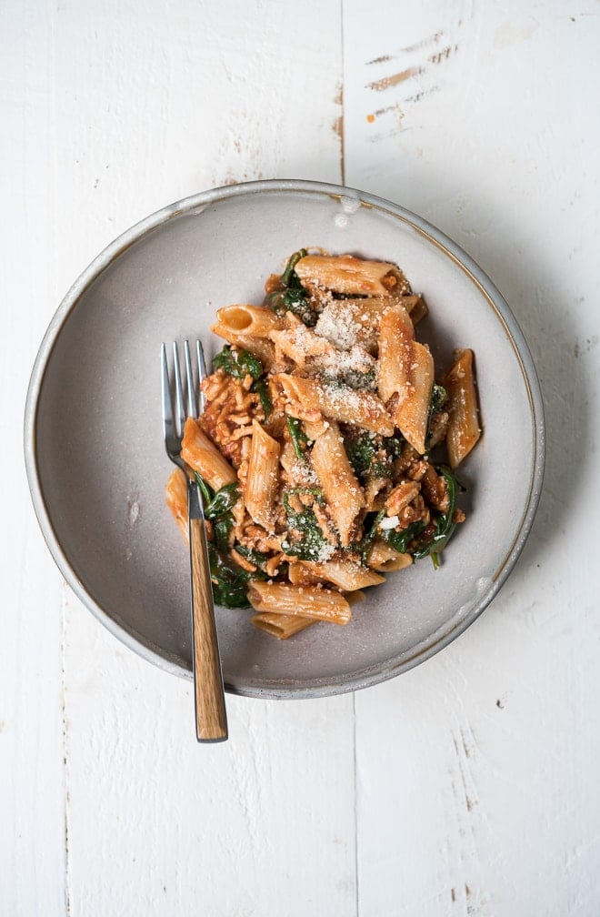 pasta in a bowl with tomato sauce, spinach and cheese with a fork on a white background
