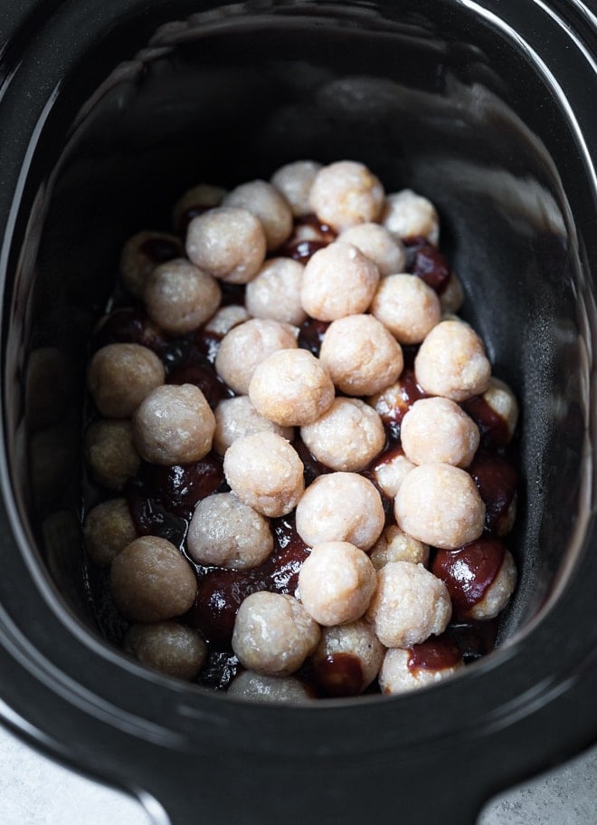 overhead shot of raw meatballs layered in a slow cooker over sauce