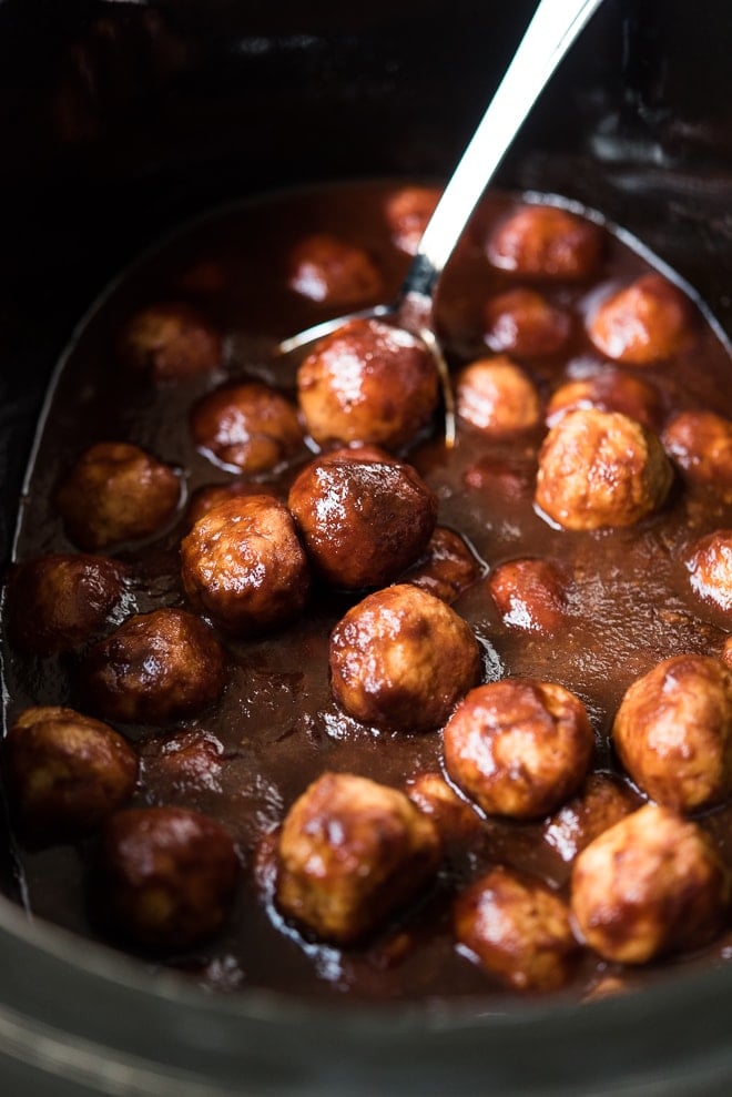 cooked meatballs in a slow cooker being scooped out with a spoon