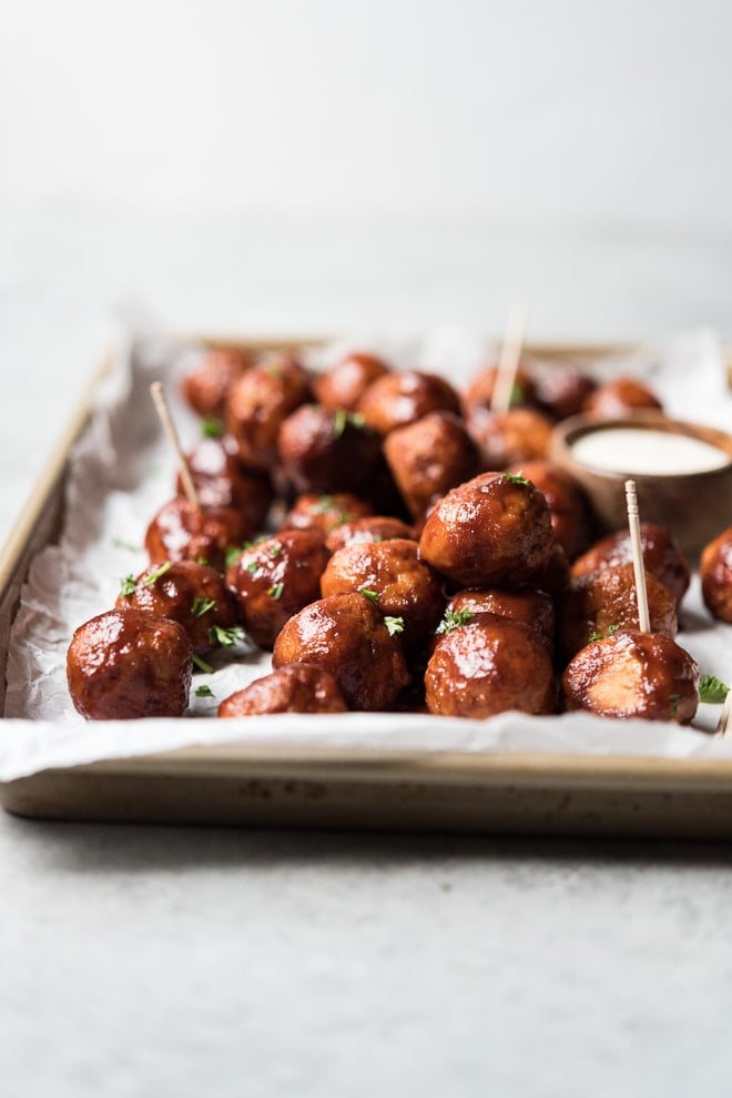 shot of meatballs piled on a sheet pan with toothpicks in the meatballs