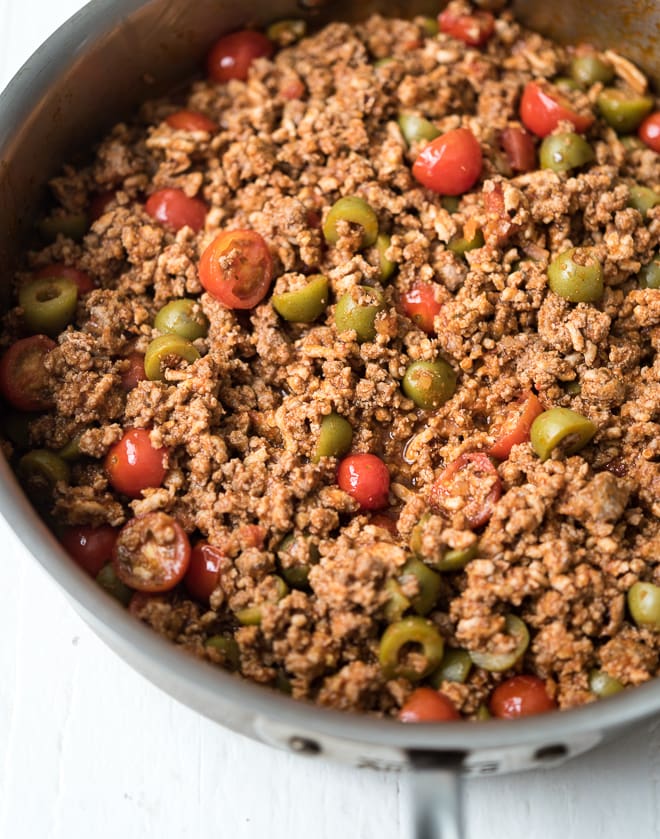 Close up of cooked ground meat in a pan with olives and tomatoes