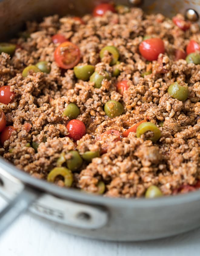 close up of cooked ground meat in a pan with olives and tomatoes